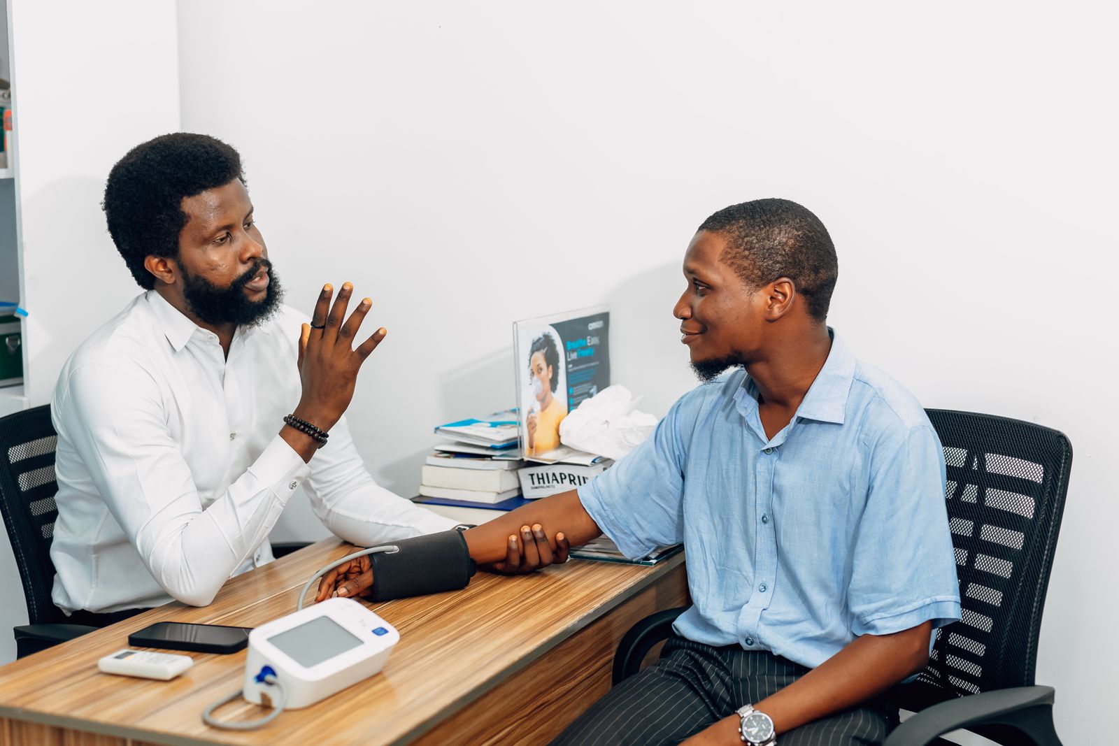 Un médecin en consultation avec un patient, tensiomètre posé sur le bureau.