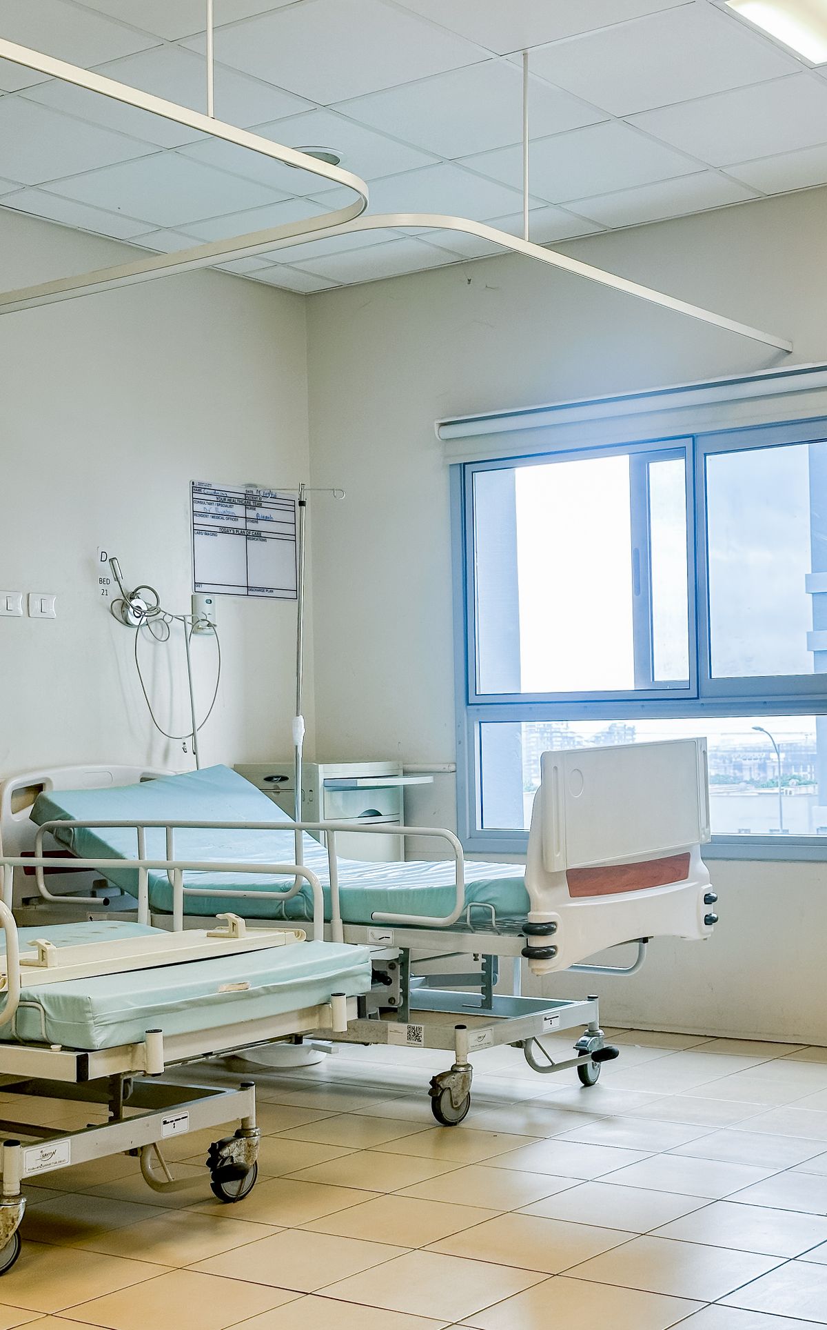 Chambre d'hospitalisation avec deux lits, vue sur la ville par la fenêtre.